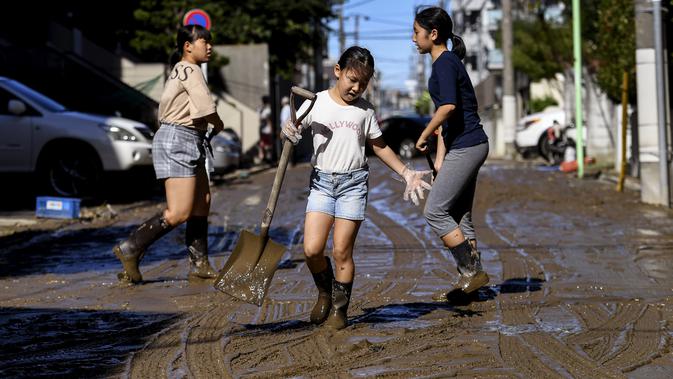 Anak-anak membersihkan lumpur dari jalan setelah banjir surut di Kawasaki, Minggu (13/10/2019). Topan dahsyat Hagibis yang menerjang sejumlah wilayah di Jepang menyebabkan banjir di beberapa lokasi. (Photo by WILLIAM WEST / AFP)
