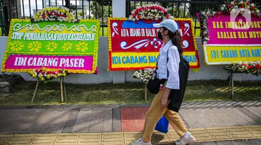 Seorang wanita melintas di depan karangan bunga yang memenuhi luar gedung DPR MPR RI, Jalan Gatot Subroto, Jakarta Pusat, Rabu(12/4/2023). (Liputan6.com/Faizal Fanani)