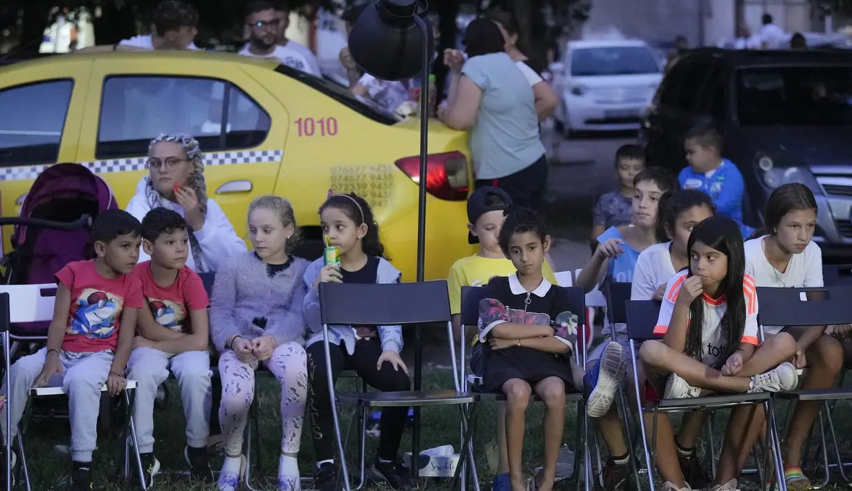 Anak-anak menyaksikan pemutaran film bertema kekerasan aparat, dalam sebuah festival 'outdoor' di Bucharest, Rumania (31/8/2021). Sejumlah film yang ditampilkan dalam festival film ini menampilkan fakta mengenai kekerasan aparat pada warga sipil. (AP Photo/ Vadim Ghirda)