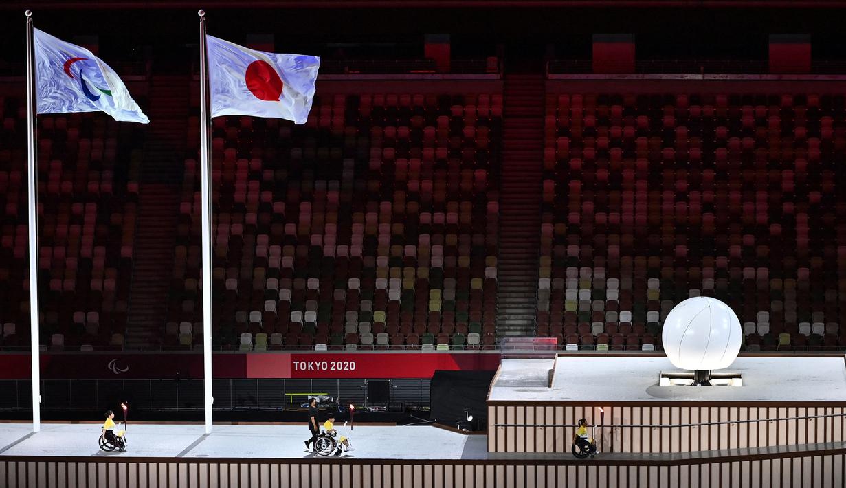 Tiga pembawa obor mengangkut api Paralimpiade sebelum menyalakan kuali (kanan) selama upacara pembukaan Paralimpiade Tokyo 2020 di Stadion Olimpiade di Tokyo pada 24 Agustus 2021. (AFP/Charly Triballeau)
