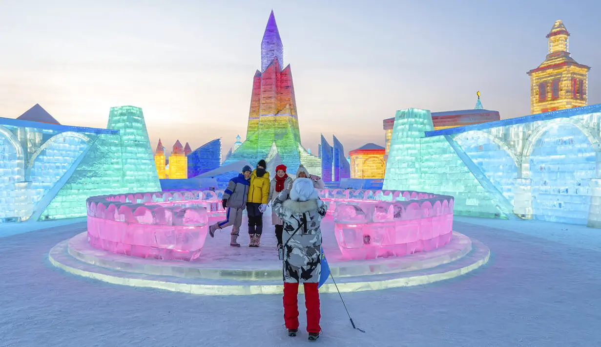 Pengunjung berpose dengan pahatan es yang dihiasi sorotan lampu warna-warni di Festival Dunia Es dan Salju Harbin, Harbin, Provinsi Heilongjiang, China, Selasa (5/1/2021). Festival yang berlangsung tahunan ini adalah festival salju dan es terbesar di dunia. (Chinatopix via AP)