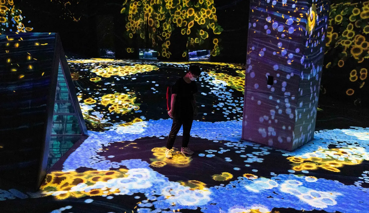 Seorang anggota staf berjalan melalui instalasi digital interaktif bernama "Shifting Valley, Living Creatures of Flowers, Symbiotic Lives" selama pratinjau media "teamLab Forest" di gedung hiburan BOSS E・ZO FUKUOKA di Fukuoka, Jepang, Jumat (16/7/2021). (YUKI IWAMURA/AFP)