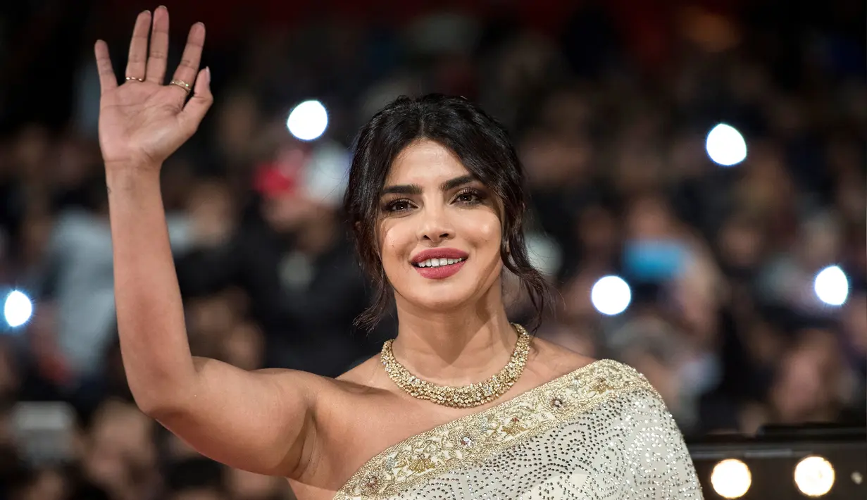 Aktris Priyanka Chopra menyapa penggemarnya saat tiba menghadiri Festival Film Internasional Marrakech ke-18 di Jemaa El Fnaa, Marrakech (5/12/2019). Priyanka Chopra tampil cantik memesona mengenakan busana sari emas dan brokat perak denga dengan kalung emas di lehernya. (AFP/Fadel Senna)