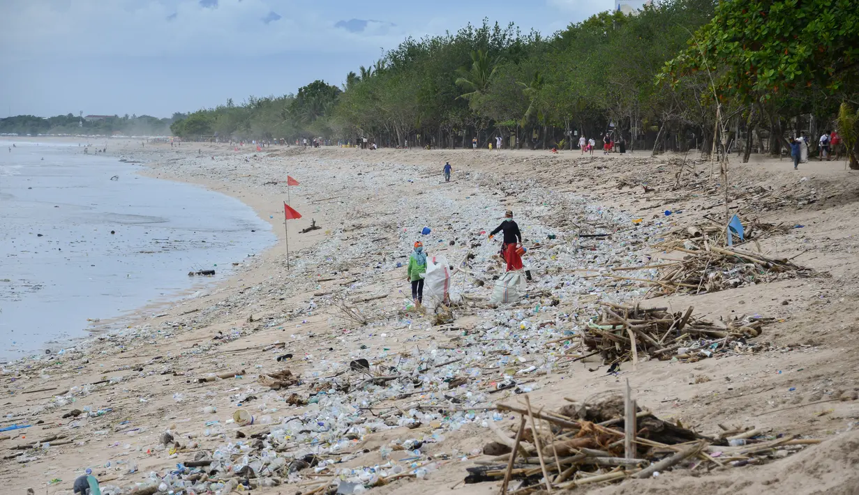 Orang-orang berjalan di antara sampah terdampar di pantai Kuta, Bali, Kamis (31/12/2020). Pantai Kuta tampak sepi menyusul aturan larangan pesta perayaan pergantian tahun baru dan pemberlakuan jam malam untuk pengendalian aktivitas masyarakat yang dibatasi. (SONNY TUMBELAKA / AFP)