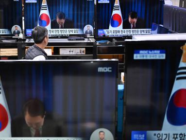 Seorang penjaga toko menyaksikan layar televisi yang menampilkan siaran langsung Presiden Korea Selatan Yoon Suk Yeol yang membungkuk setelah mengakhiri pidatonya, di sebuah pasar elektronik di Seoul pada Sabtu 7 Desember 2024. (Jung Yeon-je/AFP)