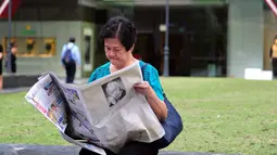 Seorang wanita membaca koran setelah sehari meninggalnya mantan PM Singapura, Lee Kuan Yew, Singapura, Selasa (24/3/2015). Lee meninggal pada hari Senin (23/3) di usia 91 tahun dan wajahnya menghiasi berbagai media cetak Singapura. (AFP PHOTO/Mohd FYROL)