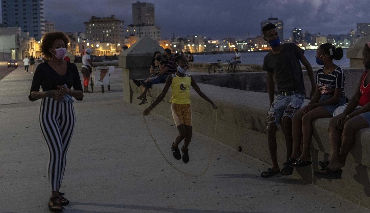 Seorang gadis bermain lompat tali sementara orang lain menghabiskan sore hari di Malecon di Havana, Kuba, pada Rabu (29/9/2021). Pihak berwenang di Kuba mulai melonggarkan pembatasan COVID-19 di beberapa kota seperti Havana dan Varadero. (AP Photo/Ramon Espinosa)