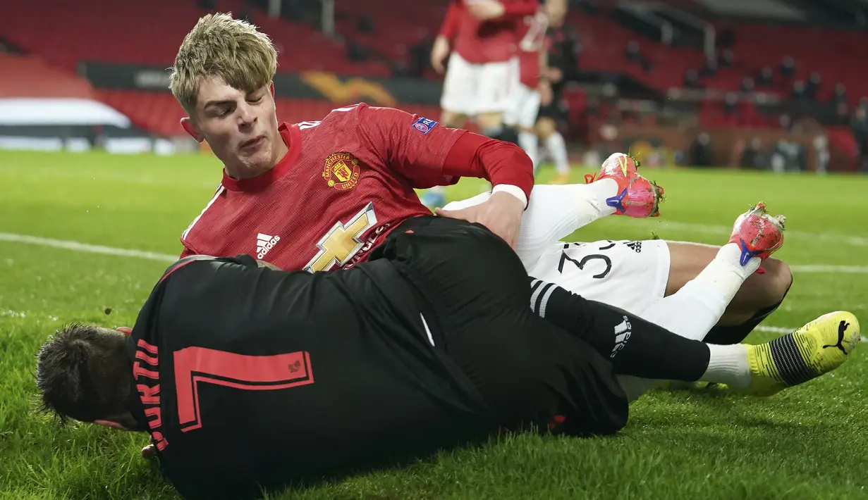 Gelandang Manchester United, Brandon Williams (atas) dan gelandang Real Sociedad, Portu terjatuh usai perebutan bola dalam laga leg kedua babak 32 Besar Liga Europa 2020/21 di Old Trafford Stadium, Kamis (25/2/2021). Manchester United bermain imbang 0-0 dengan Real Sociedad. (AP/Dave Thompson)