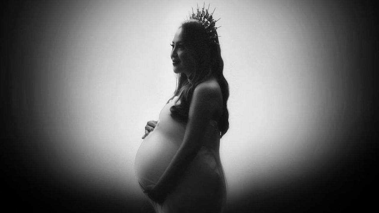 Foto hitam putih yang diambil dari samping memberikan kesan klasik dan misterius, menampilkan baby bump di perut Mpok Alpha yang tengah hamil anak kembar.<br>