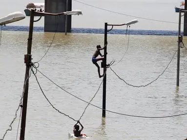 Warga memanjat tiang listrik saat terjebak banjir di tepi sungai Gangga, Allahabad, India, (21/8). Banjir bandang menerjang sejumlah wilayah di India yang menyebabkan banyak warga yang terjebak. (REUTERS/Jitendra Prakash)