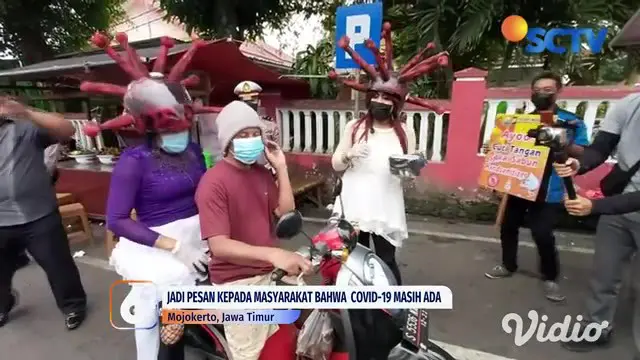 Nampak terlihat dua orang waria yang menggunakan helm berkarakter virus corona, mencegat para pengendara, pedagang, dan pejalan kaki di kawasan jalan raya menuju tempat wisata Pacet, Kabupaten Mojokerto, Jawa Timur.