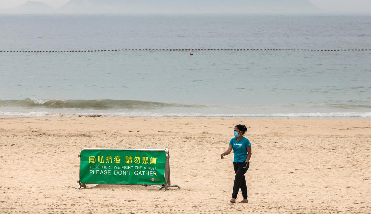 Seorang wanita berjalan melewati papan petunjuk saat para pekerja mulai menutup Pantai Shek O di Hong Kong, Kamis (17/3/2022). Pemerintah Hong Kong mengatakan akan menutup pantai umum untuk mengekang penyebaran virus corona COVID-19. (DALE DE LA REY/AFP)