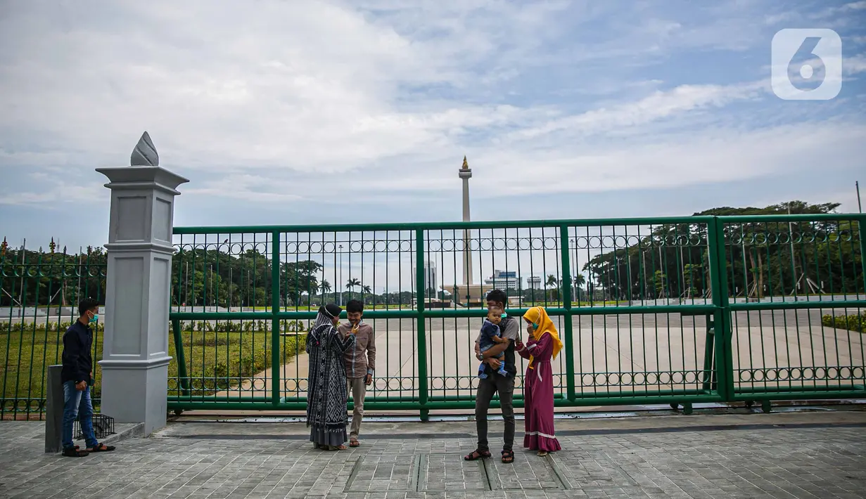 Warga berfoto di belakang Monumen Nasional atau Monas di Jakarta, Jumat (1/1/2021). Selain Monas, Taman Margasatwa Ragunan juga ditutup saat libur Tahun Baru. (Liputan6.com/Faizal Fanani)
