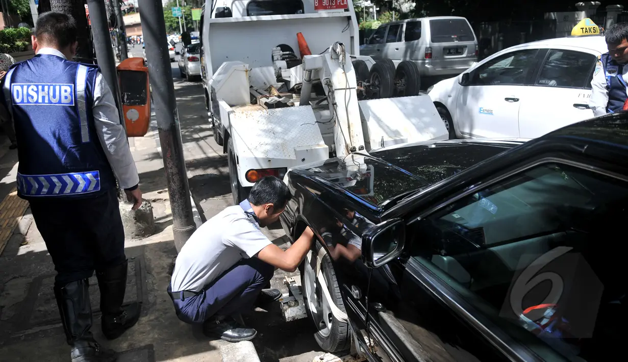 Petugas Dishub memasang alat derek pada kendaraan yang parkir liar di kawasan Cikini, Jakarta, Selasa (28/4/2015). Masih banyak mobil pribadi yang parkir disembarang tempat.(Liputan6.com/JohanTallo)