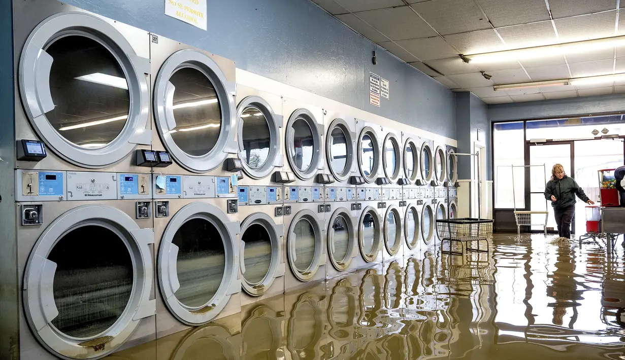 Pamela Cerruti berjalan melewati Pajaro Coin Laundry saat banjir mengelilingi mesin-mesin di komunitas Pajaro di Monterey County, California, Selasa, 14 Maret 2023.  (AP Photo/Noah Berger)