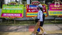 Seorang wanita melintas di depan karangan bunga yang memenuhi luar gedung DPR MPR RI, Jalan Gatot Subroto, Jakarta Pusat, Rabu(12/4/2023). (Liputan6.com/Faizal Fanani)