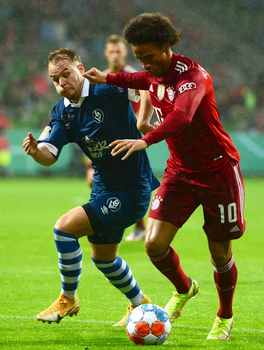 Gelandang Bayern Munchen, Leroy Sane membawa bola dari kawalan pemain Bremen SV, Mats Kaiser dalam laga putaran pertama DFB Pokal 2021-22 di Bremen, Jerman utara (25/8/2021). Munchen menang telak atas Bremen SV dengan skor 12-0. (AFP/Patrik Stollarz)