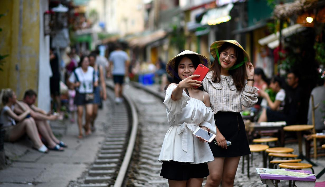 Foto pada 8 Juni 2019 menunjukkan dua orang wanita berswafoto di tengah jalur kereta api populer di Hanoi, Vietnam. Turis sengaja datang ke Old Quarter untuk berfoto di rel kereta api yang dianggap ' instagramable' tersebut. (Photo by Manan VATSYAYANA / AFP)