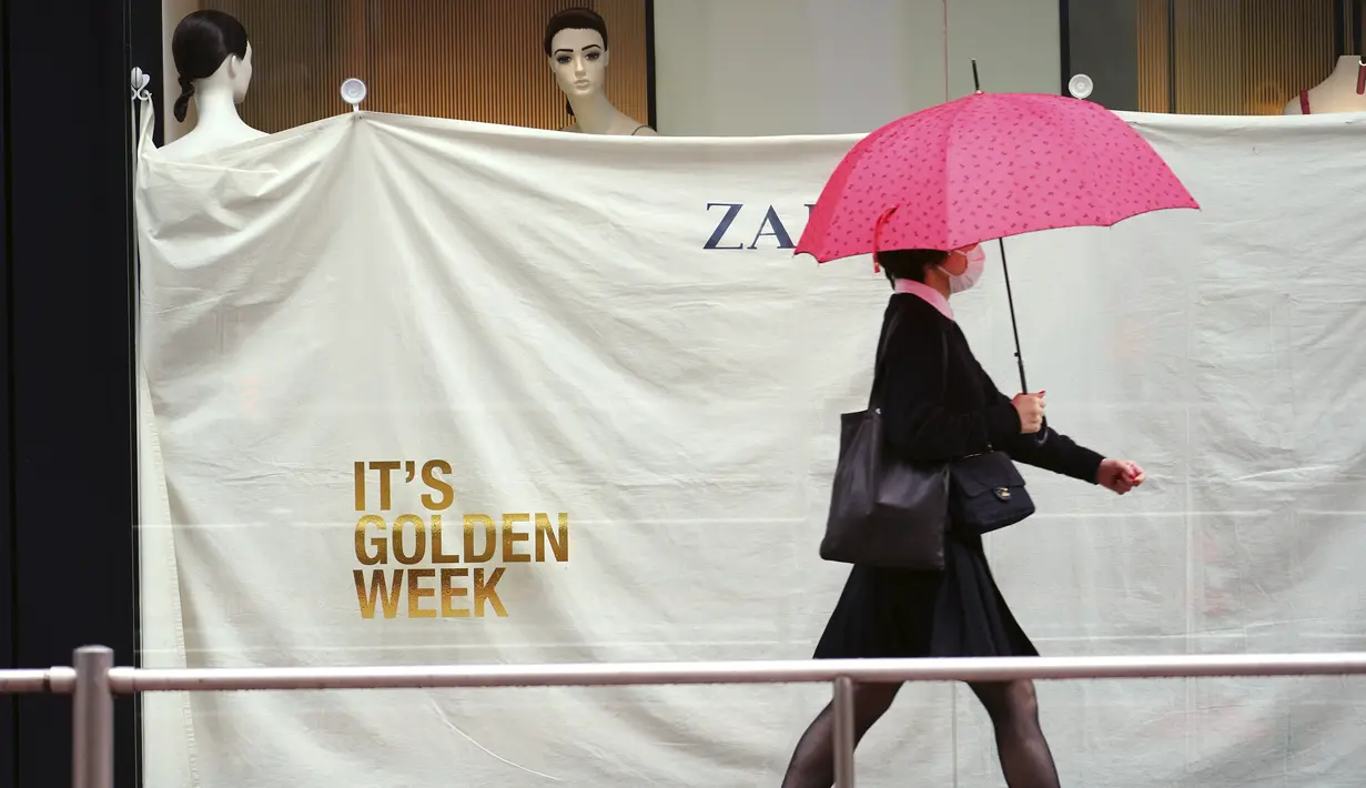 Seorang wanita yang mengenakan masker pelindung untuk membantu mengekang penyebaran virus corona berjalan di dekat jendela toko pakaian pada awal liburan "Minggu Emas" Jepang di distrik Shibuya, Tokyo, Kamis (29/4/2021). (AP Photo/Eugene Hoshiko)