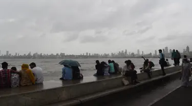 Warga India duduk di pinggir laut ketika awan gelap menyelimuti langit Mumbai (12/6/2019). Badai siklon vayu melesat ke arah barat India telah diperkuat dengan hembusan angin hingga 170 kilometer per jam (105 mph) yang diperkirakan akan menerjang pada 13 Juni 2019. (AFP Photo/Punit Paranjpe)