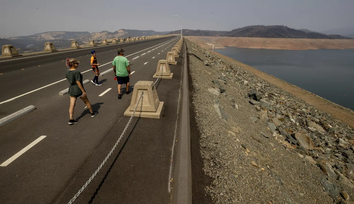 Pejalan kaki berjalan melintasi Bendungan Oroville di Area Rekreasi Danau Oroville saat kondisi kekeringan berlanjut di Butte County, California, Minggu (228/2021). Kekeringan ekstrem di California telah membuat ketinggian air di danau tersebut terus menurun. (AP Photo/Ethan Swope)