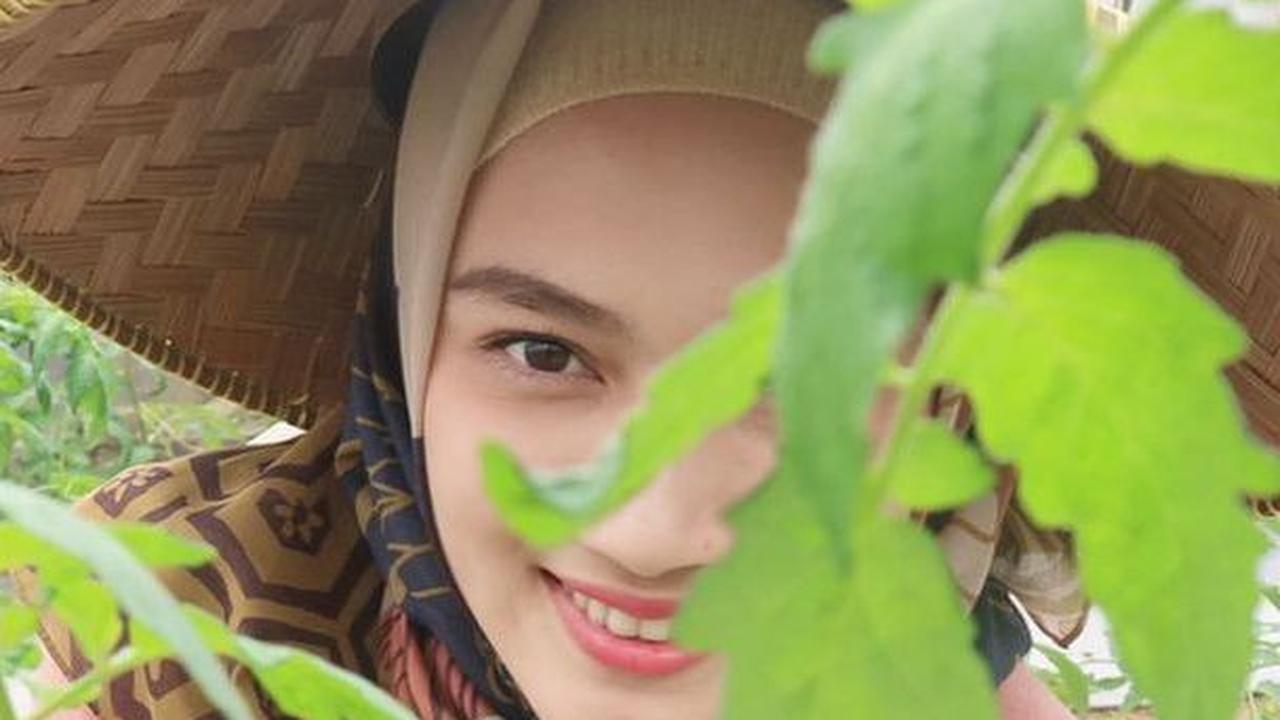 Melody Laksani terlihat sedang menanam tomat. Untuk tampil beda, ia memilih menggunakan caping tani.