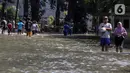 Warga melintasi genangan air yang merendam jalan di kawasan Kampung Makasar, Jakarta Timur, Senin (7/7/2025). (Liputan6.com/Herman Zakharia)