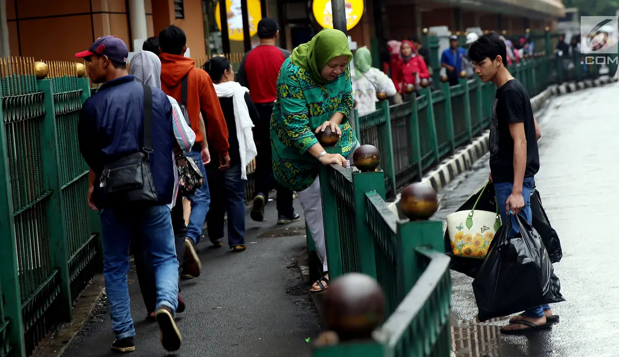Seorang ibu berusaha melompati pagar pembatas di Stasiun Cikini, Jakarta Pusat, Rabu, (20/12). Akses pintu keluar stasiun yang terlalu jauh membuat banyak penumpang yang mencari jalan pintas dengan melompat pagar. (Liputan6.com/Johan Tallo)