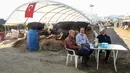 Para pria menunggu pembeli hewan kurban di pasar darurat yang didirikan oleh Kotamadya Yenimahalle menjelang hari raya Idul Adha di lingkungan Yakacik, Ankara, Turki, Senin (12/7/2021). Hari suci umat Muslim, Idul Adha dilaksanakan dengan menyembelih hewan kurban. (Adem ALTAN / AFP)
