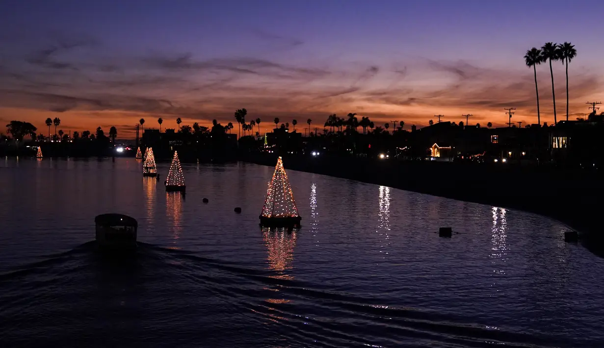 Perahu melewati lampu pohon Natal yang mengapung di Long Beach, California, Minggu (19/12/2021). Sambut Natal, pantai di California menghiasi pantainya dengan hiasan lampu pohon Natal. (AP Photo/Ashley Landis)