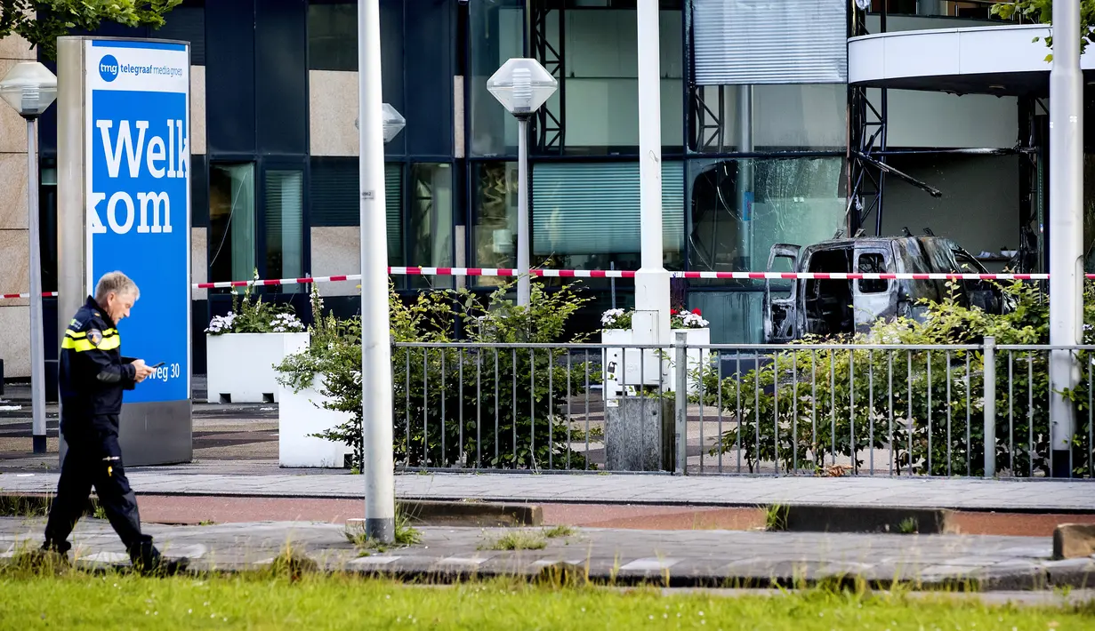 Seorang polisi berjalan dekat sebuah mobil van yang menabrak pintu depan gedung tempat surat kabar ternama Belanda, De Telegraaf di Amsterdam, Selasa (26/6). Akibatnya mobil van itu terbakar dan menyebakan kerusakan pada gedung. (KOEN VAN WEEL/ANP/AFP)