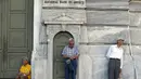 Pensiunan menunggu di depan pintu masuk Bank Nasional untuk menerima bagian dari dana pensiun mereka di Athena, Yunani (9/7/2015). Banyak bank di Yunani tutup dan penarikan uang tunai dari ATM dibatasi hanya 67 dolar sehari. (REUTERS/Jean Paul Pelissier)
