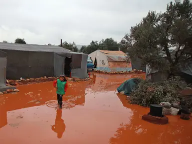 Seorang gadis berjalan melewati genangan air hujan di depan tenda di kamp untuk warga Suriah yang kebanjiran di dekat desa Killi di utara provinsi barat laut Idlib (5/12/2019). (AFP Photo/Aaref Watad)