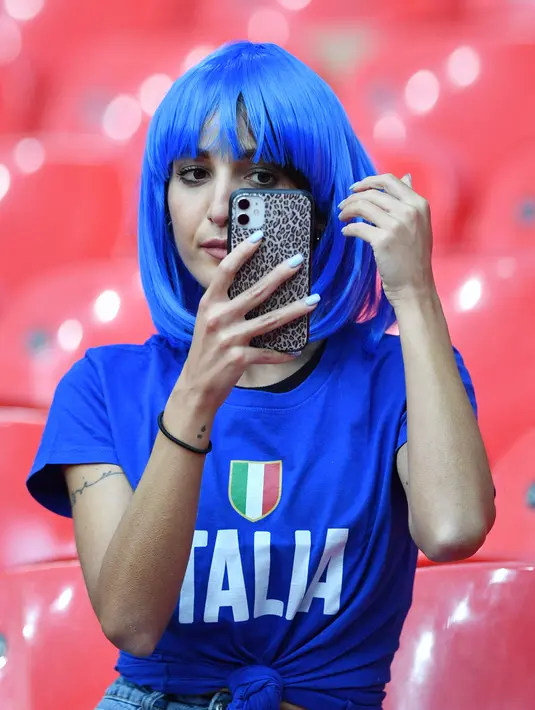 Fans wanita Italia melihat ponsel sambil merapikan rambutnya sebelum pertandingan semifinal EURO 2020 antara Italia dan Spanyol di Stadion Wembley di London (7/7/2021). (AFP/Pool/Justin Tallis)