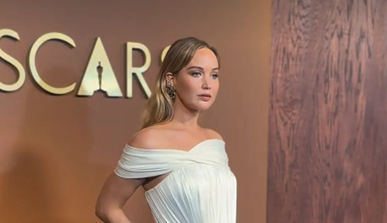 Jennifer Lawrence tampil bak dewi dengan pleated gown dari Dior. Gaun putih off shoulder itu memiliki slit yang elegan [@theacademy]