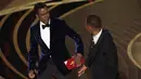 Reaksi presenter Chris Rock setelah dipukul oleh Will Smith di atas panggung Piala Oscar 2022 saat penghargaan untuk film dokumenter terbaik di Dolby Theatre, Minggu (27/3/2022). Will Smith merasa lawakan sang komedian terkait istrinya, Jada Pinkett Smith keterlaluan. (AP Photo/Chris Pizzello)