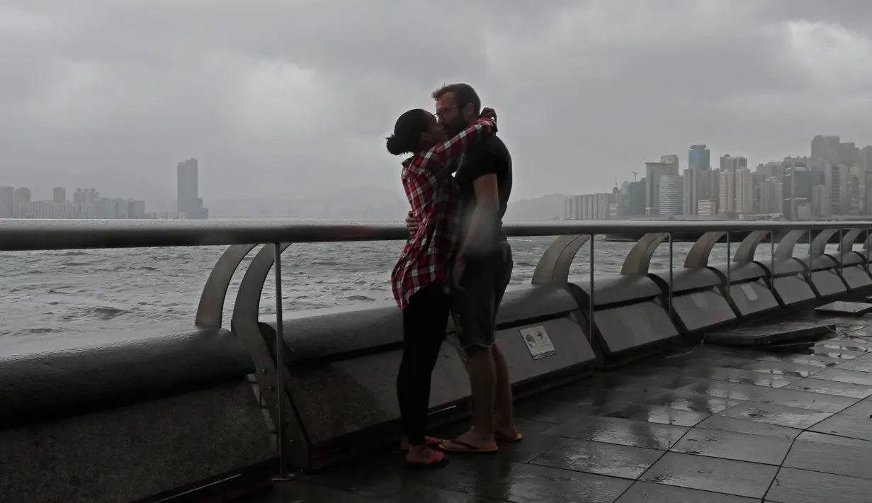 Warga berciuman saat angin kencang yang disebabkan oleh angin topan Hato menerjang tepi pantai Victoria Habour di Hong Kong, (23/8). Terjangan topan Hato mengakibatkan lebih dari 400 penerbangan dibatalkan. (AP Photo/Vincent Yu)