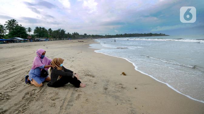 Wisatawan yang mengenakan masker menikmati suasana Pantai Anyer di Cilegon, Banten, Minggu (25/10/2020). Akhir pekan dimanfaatkan warga Jakarta dan sekitarnya untuk berwisata dengan tetap menerapkan protokol kesehatan Covid-19. (merdeka.com/Arie Basuki)