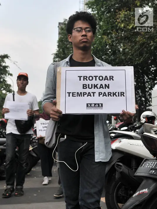 Anggota Koalisi Pejalan kaki menyelipkan selebaran di salah satu sepeda motor yang parkir di trotoar depan GBK, Jakarta, Minggu (9/12). Aksi tersebut dalam rangka menyadarkan masyarakat tentang pelanggaran parkir liar. (Merdeka.com/Iqbal S. Nugroho)