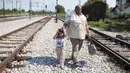 Seorang imigran bersama anaknya berjalan menyusuri rel kereta api saat perjalanan menuju Gevgelija, wilayah perbatasan Macedonia-Yunani, Kamis (9/7). Mereka menempuh ribuan kilometer agar dapat mengejar kereta tujuan Serbia (AFP PHOTO/Robert ATANASOVSKI)