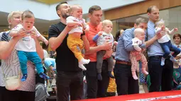Sejumlah bayi didampingi ayah mereka bersiap mengikuti lomba merangkak untuk memperingati Hari Anak Internasional di Vilnius, Lithuania, Kamis (1/6). Orang tua memberikan iming-iming benda kesukaan buah hatinya saat mengikuti lomba. (Petras Malukas/AFP)