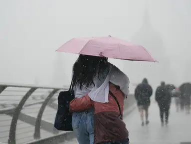 Orang-orang dengan payung berjalan di tengah hujan di Jembatan Milenium, London, Rabu (17/8/2022). Setelah berminggu-minggu cuaca terik, yang telah menyebabkan kekeringan dan membuat tanah kering, peringatan badai petir kuning dari Kantor Meteorologi memperkirakan hujan lebat dan badai petir yang bisa melanda bagian Inggris dan Wales. (Victoria Jones/PA via AP)
