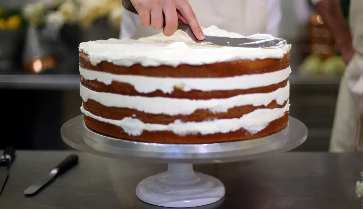 Pemilik Violet Bakery, Claire Ptak memberi sentuhan akhir pada kue pengantin Pangeran Harry dan Meghan Markle di dapur Istana Buckingham, London, Kamis (17/5). Harry dan Meghan akan menikah pada 19 Mei mendatang di Windsor Castle. (HANNAH MCKAY/POOL/AFP)