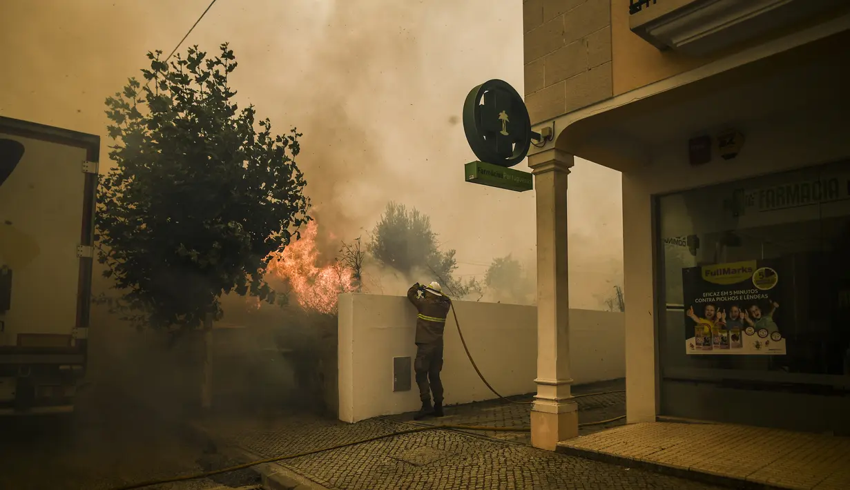 Seorang Pemadam Kebakaran berusaha memadamkan api di desa Cardigos di Macao, Portugal tengah (21/7/2019).  Kebakaran hutan tersebut memaksa penduduk desa dievakuasi ketempat yang lebih aman. (AFP Photo/Patricia De Melo Moreira)
