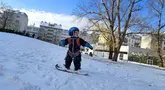 Seorang anak laki-laki berusia dua tahun bermain papan seluncur salju di taman Steinhage di Wina, Austria pada 3 Desember 2023. (Joe Klamar / AFP)