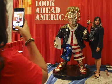 Seorang perempuan berfoto dengan patung emas Donald Trump pada Konferensi Politik Konservatif (CPAC) di Orlando, Florida, Jumat (26/2/2021). Kemunculan patung emas yang lebih besar dari ukuran pria dewasa di acara tersebut menjadi viral. (Sam Thomas/Orlando Sentinel via AP)
