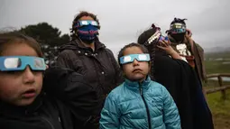Keluarga Adat Mapuche menggunakan kacamata khusus untuk mencoba mengamati gerhana matahari total di Carahue, La Araucania, Chile, Senin (14/12/2020). Gerhana matahari total terlihat dari Chile dan wilayah Patagonia utara Argentina. (AP Photo/Esteban Felix)
