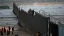 Dua imigran Honduras mengangkangi perbatasan yang memisahkan Meksiko dari AS di Tijuana, Meksiko, Rabu (21/11). Wali Kota Tijuana mendeklarasikan krisis kemanusiaan di perbatasan kotanya dengan AS. (AP Photo/Ramon Espinosa)