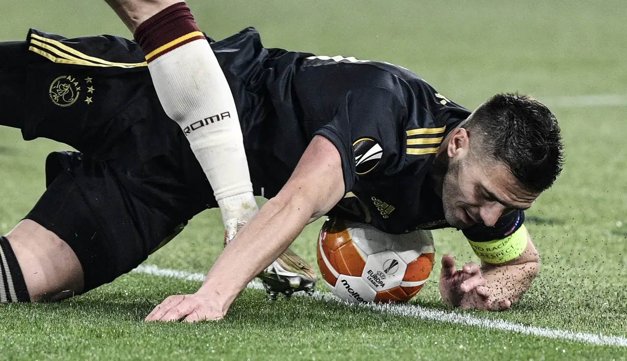 Striker Ajax Amsterdam, Dusan Tadic terjatuh usai ditekel pemain AS Roma dalam laga leg kedua perempatfinal Liga Europa 2020/2021 di Olimpico Stadium, Roma, Kamis (15/4/2021). Ajax bermain imbang 1-1 dengan AS Roma. (AFP/Filippo Monteforte)