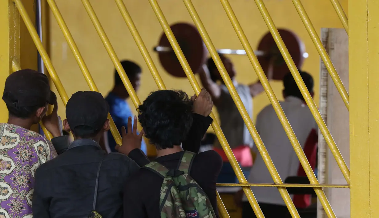 Warga menonton Atlet Angkat Besi berlatih dekat halaman Parkir Angkat Besi di Senayan, Jakarta, Senin (11/1/2016). Hal ini karena tempat Latihan dalam tahap renovasi. (Bola.com/Nicklas Hanoatubun)